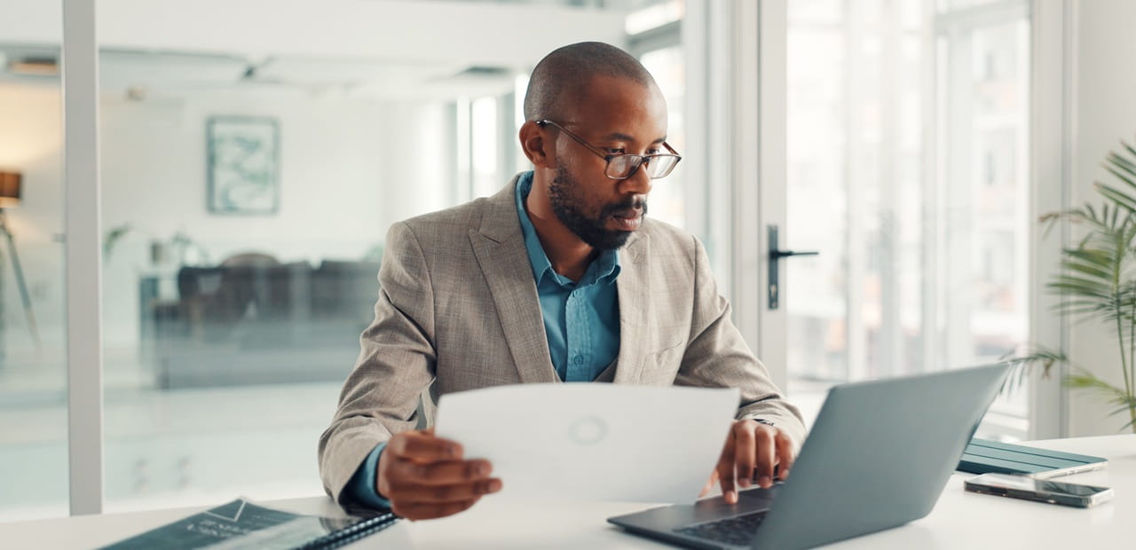 Business owner reviewing financial documents and working on a laptop, illustrating management of an owner-only 401(k) retirement plan for a self-employed professional.