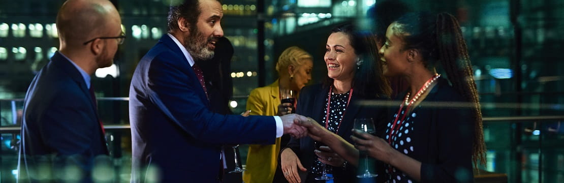 Group of four professionals stands behind a glass wall talking.